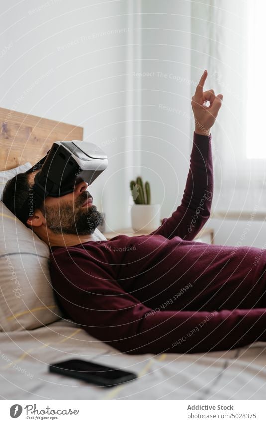 Male interacting with virtual reality on bed man vr point high tech goggles headset explore lying bedroom simulate experience glasses male gadget futuristic guy
