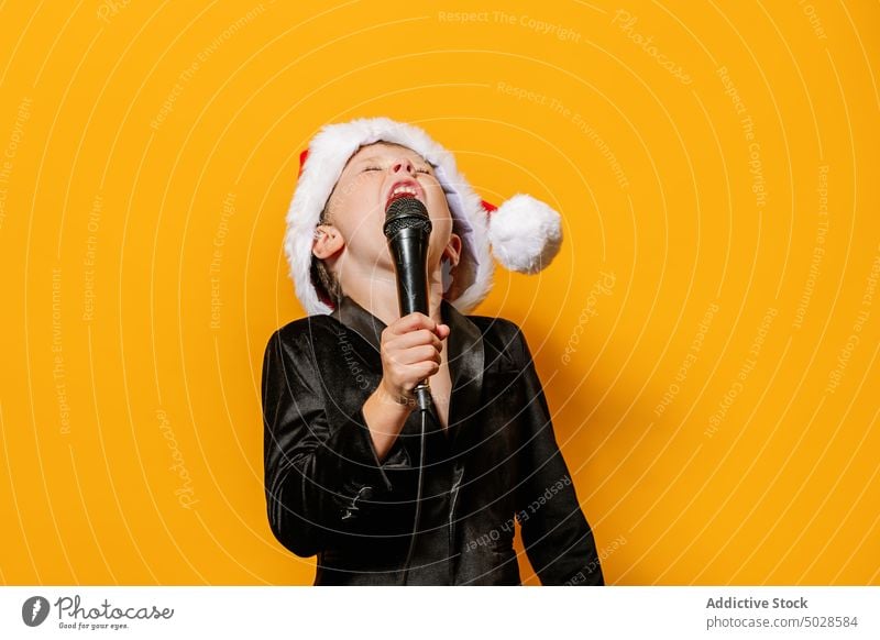 Boy singing loud Christmas song boy christmas microphone celebrate holiday colorful bright kid scream singer eyes closed voice vibrant mouth opened festive