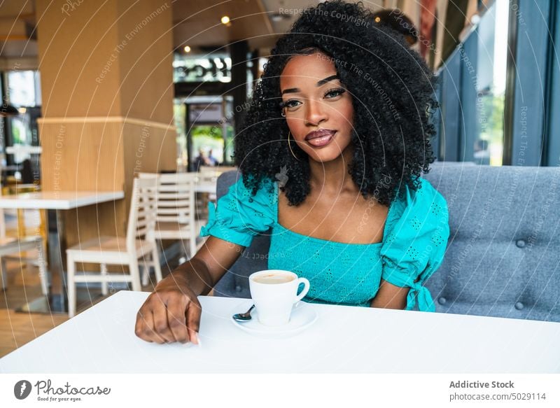 Black woman with coffee in cafeteria table chill coffee shop hot drink restaurant content makeup beverage female charming sit black ethnic african american lady