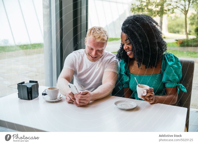 Cheerful multiracial couple sitting in cafe using mobile phone date cafeteria relationship meeting browsing together friend coffee chill multiethnic cheerful