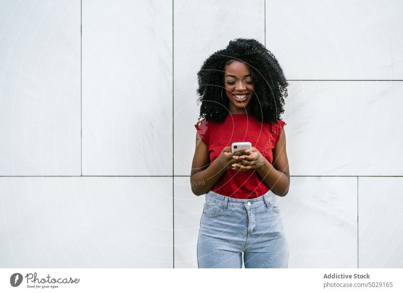 Cheerful African American woman browsing on smartphone near wall cheerful smile cellphone phone call street happy style device conversation gadget mobile