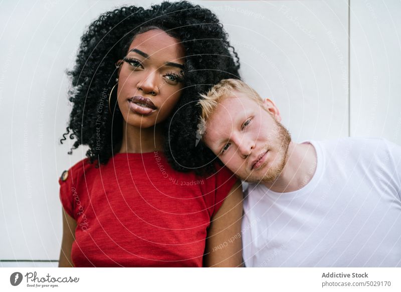 Unemotional diverse couple standing near wall boyfriend girlfriend lean on unemotional emotionless hug relationship tile together serious young multiethnic
