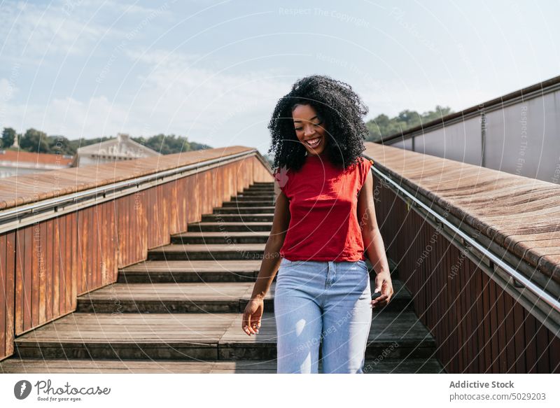 Cheerful ethnic woman walking on wooden stairs smile happy stairway city street outfit afro urban female african american young black curly hair casual outside