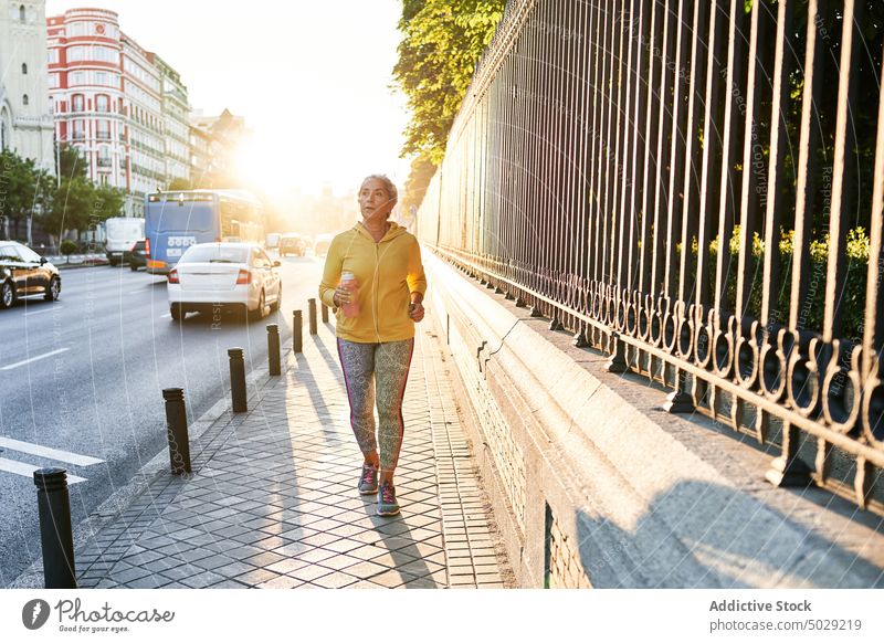 Elderly female athlete running on street sportswoman sunrise cardio fitness training pavement morning exercise wellness wellbeing breathe energy activity runner