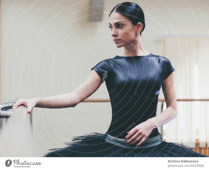 Ballerina in black tutu and pointe stretches on barre in ballet gym. Woman standing near bar and mirror, preparing for perfomance. art balance ballerina