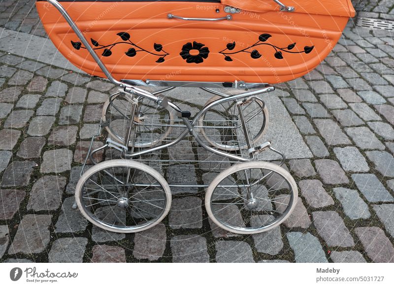 Old baby carriage of the fifties in orange with floral pattern on old gray cobblestones on the Oberstadtmarkt in Marburg an der Lahn in Hesse Baby carriage