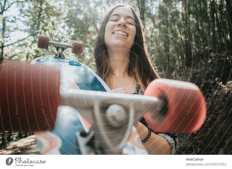 Cheerful young woman holding a long board on the road of the forest smiling to camera, risky sports person female stylish trendy youth skate fun urban cool
