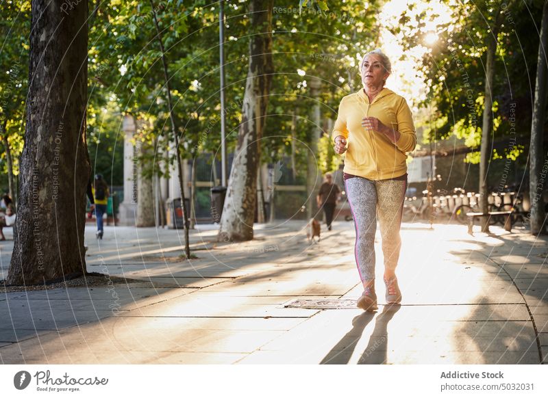 Elderly female athlete running on street sportswoman sunrise cardio fitness training pavement morning exercise wellness wellbeing breathe energy activity runner