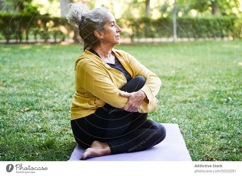 Aged woman stretching during yoga session park twist summer mat asana calm female elderly senior aged practice energy retire barefoot sit stress relief
