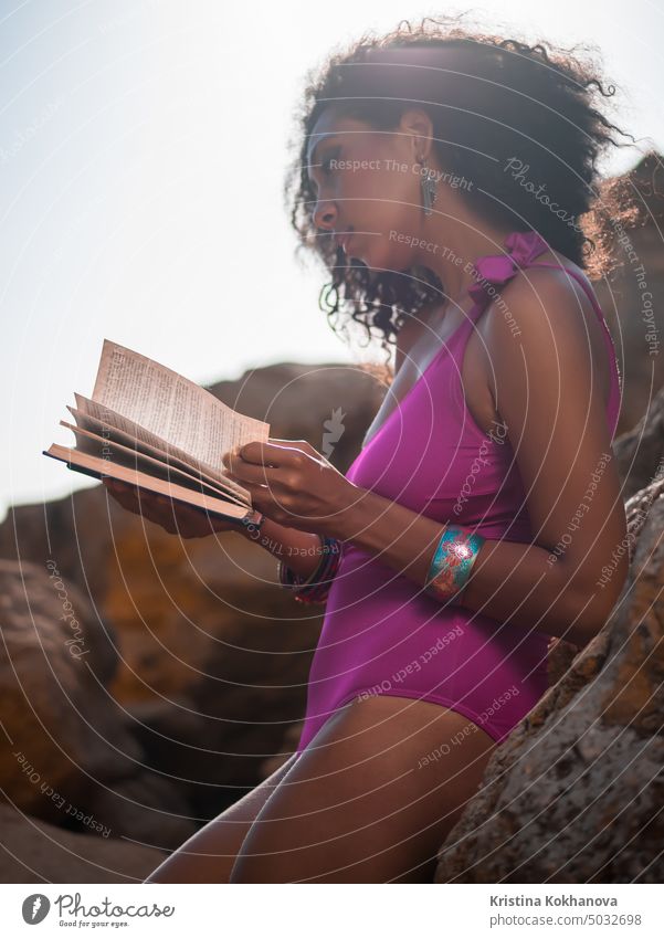 Beautiful African woman reading book on the rocks beach, pretty black female enjoying summer vacation relaxing outdoor young beautiful leisure girl sea african
