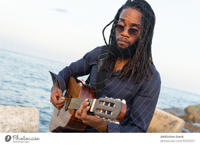 African American musician playing guitar on coast near city man guitarist chill river embankment perform acoustic male dreadlocks hobby instrument guy practice
