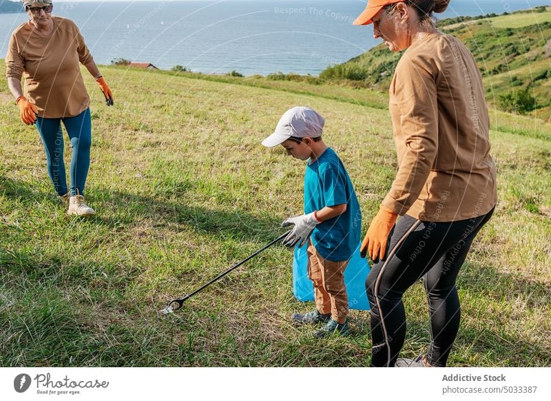 Volunteers collecting trash on grassy meadow in nature volunteer garbage environment rubbish woman boy grandmother ecology countryside litter pollute waste