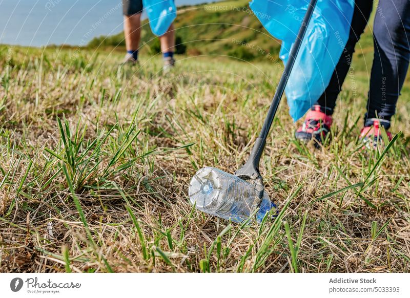 Crop volunteer picking bottle with stick in meadow collect garbage clean plastic pollute litter nature ecology environment countryside waste trash ground grass