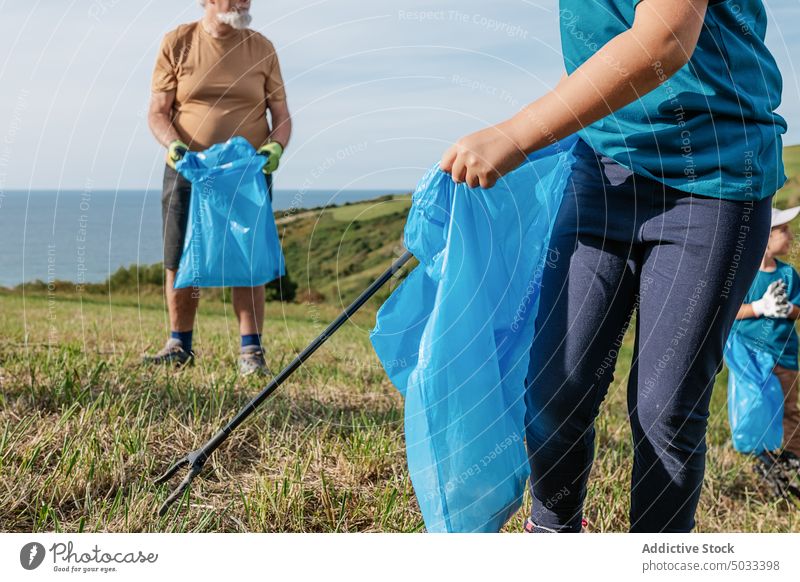 Crop girl and senior man collecting garbage on field kid boy grandfather pensioner trash tongs nature sea green volunteer child summer shore rubbish outside sun
