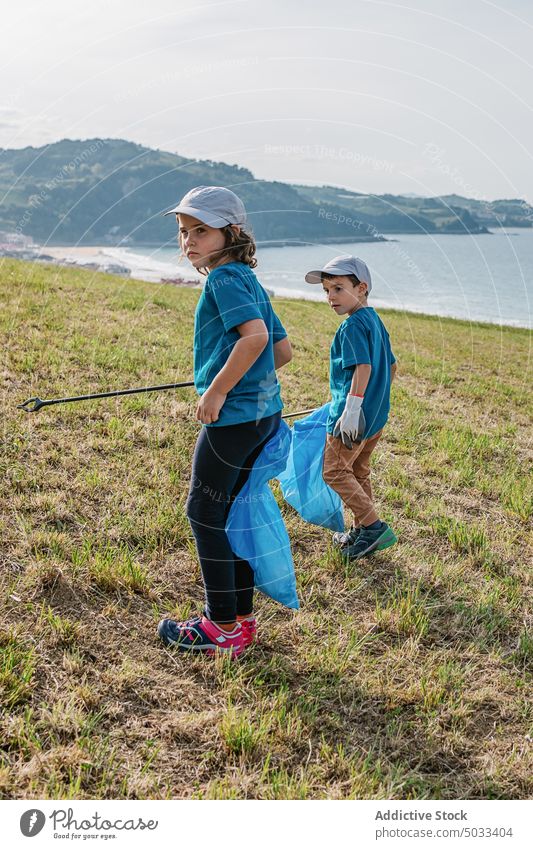 Children picking garbage on shore near sea children girl boy kid volunteer trash collect nature eco friendly environment hill recycle ecology rubbish sun green
