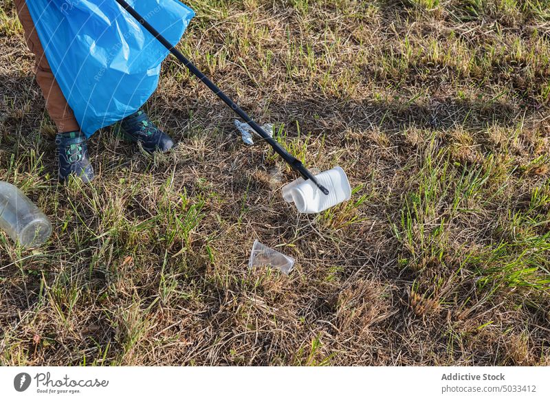 Crop volunteer picking plastic with stick in meadow plastic cup collect garbage clean pollute litter nature ecology environment countryside waste trash ground