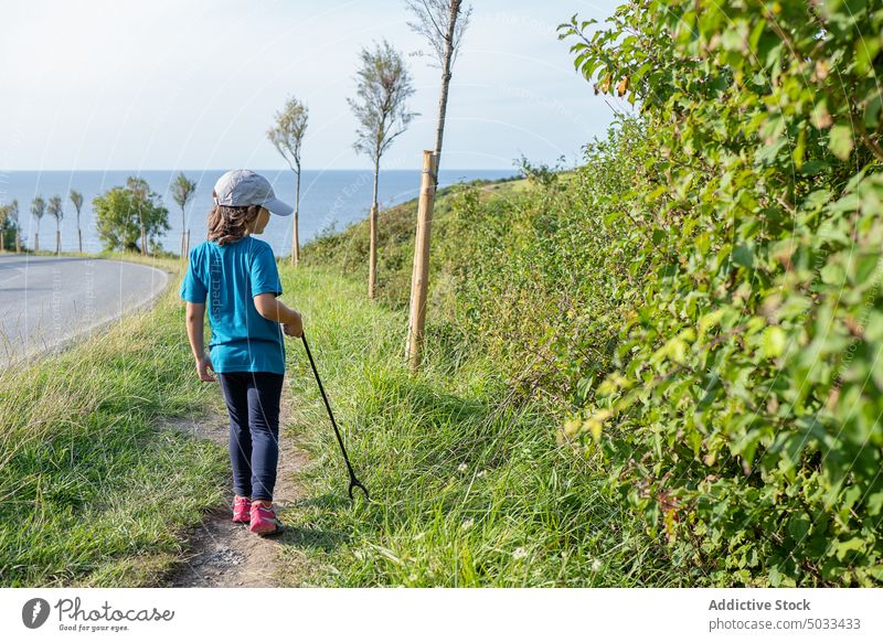 Child with trash tongs standing on green roadside kid child nature environment collect volunteer sea grass coast summer daytime childhood grassy outside shore