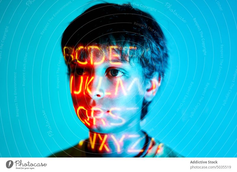 Serious boy with neon inscription on face kid portrait serious unemotional illuminate light letter orange thoughtful childhood calm pensive color emotionless