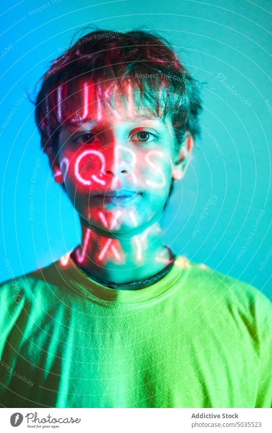 Serious boy with neon inscription on face kid portrait serious unemotional illuminate light letter orange thoughtful childhood calm pensive color emotionless