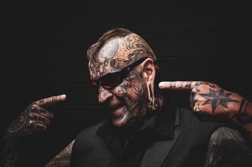 A tattooed man points fingers of right as well as left hand to draw attention to himself. Tattoo Body artist portrait moody Skin variegated body cult