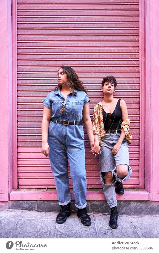 Lesbian couple leaning on pink wall women street holding hands together style girlfriend relationship madrid spain female young romantic lgbt homosexual