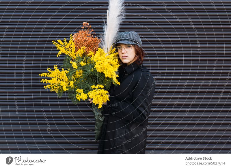 Woman with bouquet against gray wall woman flower street outerwear fresh urban style autumn female young blossom cap coat glasses daytime bloom season bunch