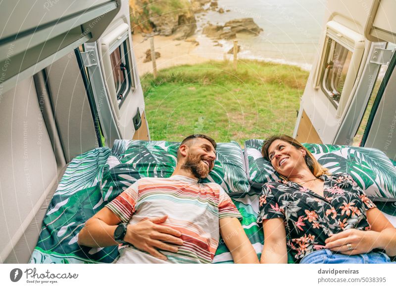 Couple looking at each other lying on the bed of their camper van happy couple looking each other landscape trip coast open door love happiness mobil home