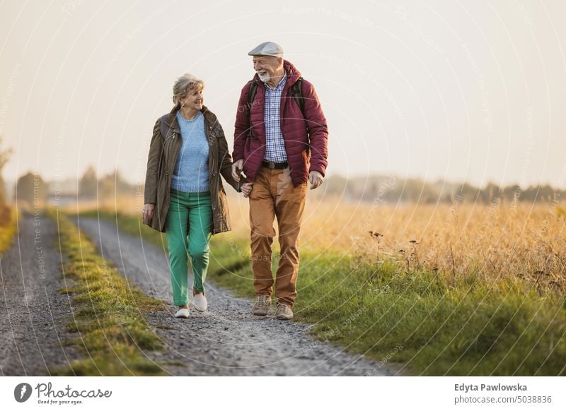 Senior couple in a field in autumn at sunset walking trip backpack senior couple woman two people mature together old retired joy love happiness adult female
