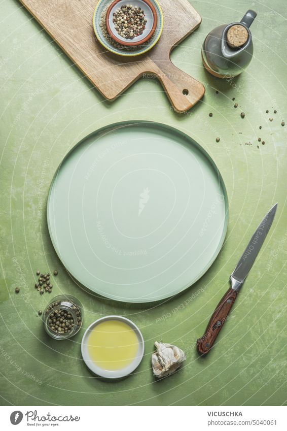 Green food background with empty plate, cutting board, knife, cooking oil and seasoning, top view. Frame green frame composition condiment culinary flat lay