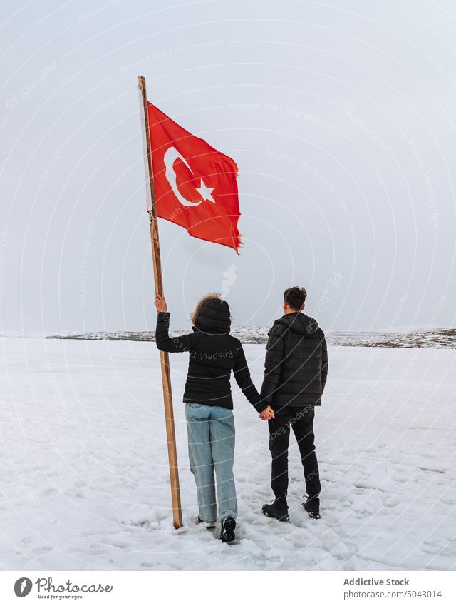 Unrecognizable traveling couple with Turkish flag holding hands on snowy terrain relationship trip tourist together nature admire national love cloudy sky