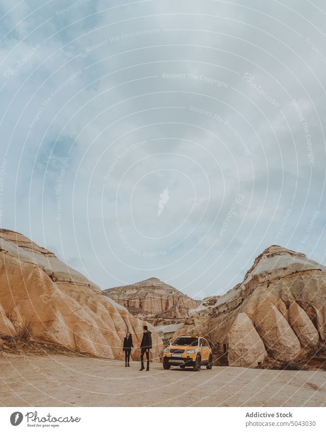 Anonymous travelers exploring desert valley with rocky formations on cloudy sky couple mountain walk wanderlust relationship car explore trip together tourism