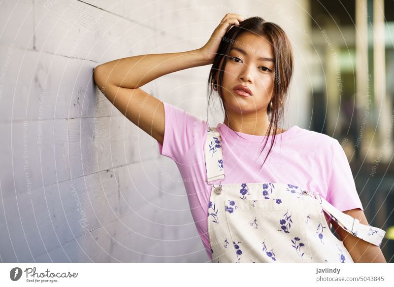 Attractive Chinese girl looking at camera with serious expression leaning against an urban wall asian chinese woman japanese fashion person office face female