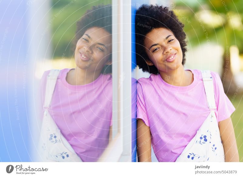 Positive black woman standing near building street city outfit style feminine window reflection happy fashion overall trendy positive house satisfied casual
