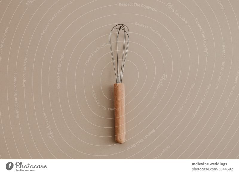 A wooden whisk beater on beige paper background. Flat lay, top view copy space. Natural light, kitchen tool. eggbeater shaker mixer metal brown object equipment