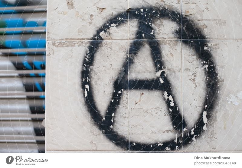 graffiti on the wall with a black anarchy symbol sign on a gray wall. Grunge wallpaper backdrop. Anarchist political graffiti artistic grungy illustration