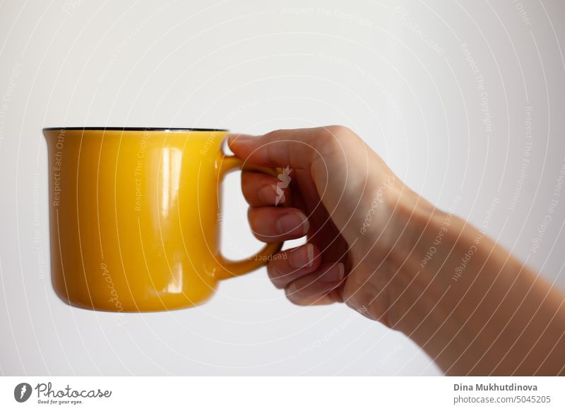Woman holding yellow cup on white background close up. Yellow mug mock up for pasting design.  Drinking coffee or tea in the morning or during break from work.