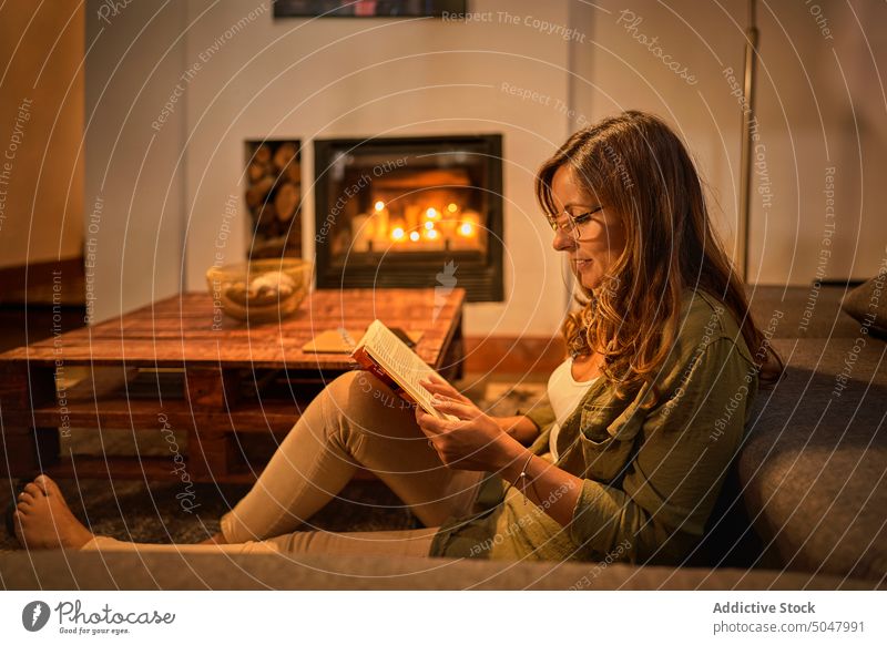 Hispanic woman reading book in evening sofa living room weekend smile interesting story female mature middle age hispanic ethnic hobby cheerful home glad chill
