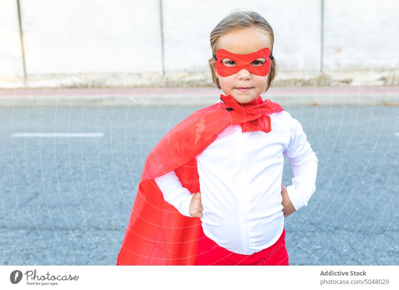 Adorable little girl in superhero outfit hand on waist brave confident cape courage cute costume kid child fearless pretend childhood bright power wall red