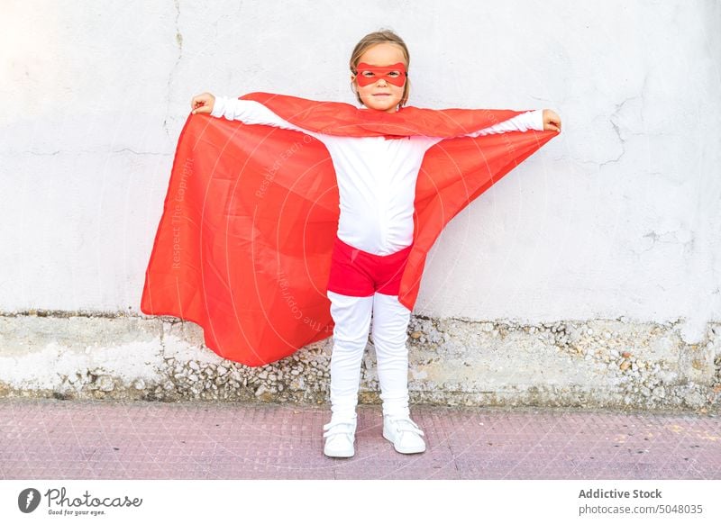 Adorable little girl in superhero outfit extended hands brave confident cape courage cute costume kid child fearless pretend childhood bright power wall red