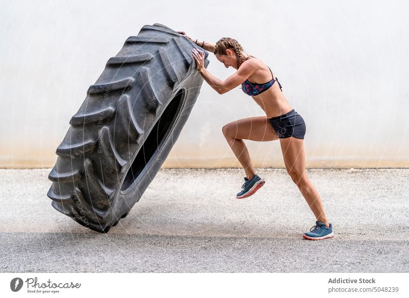 Female athlete lifting heavy tire sportswoman exercise fitness training street intense effort female huge activity strong wall power physical activewear