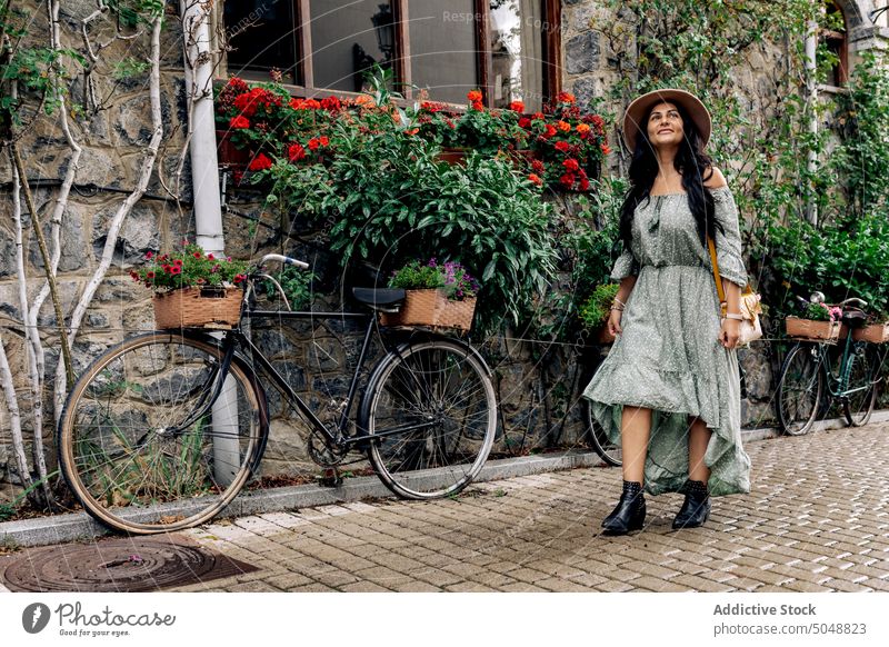 Happy female tourist walking on street woman romantic pavement explore smile stone wall bicycle building adult cheerful happy casual sunhat flower long hair