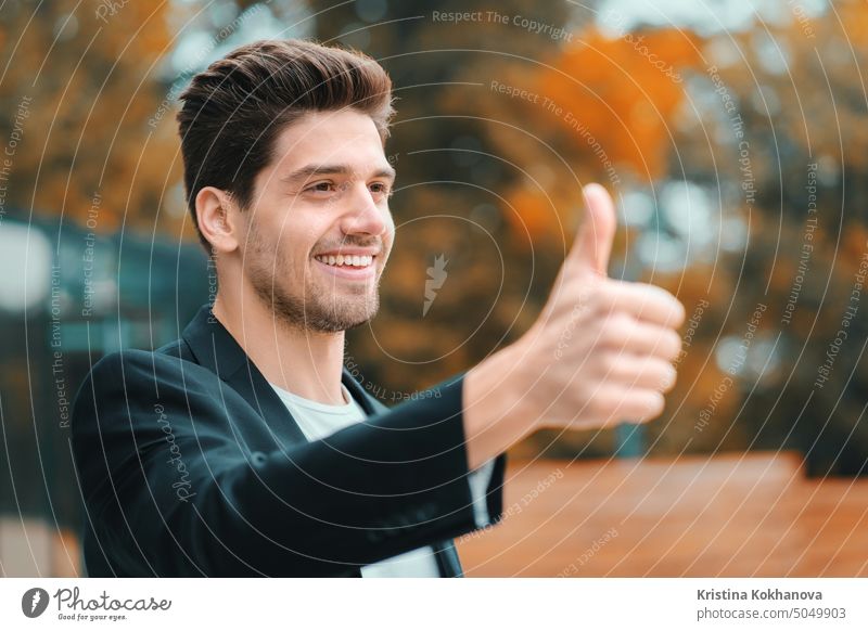 Winner. Success. Brunette young man in business clothing in office district smiles to camera and gives thumbs up. Happy guy showing gesture of approval