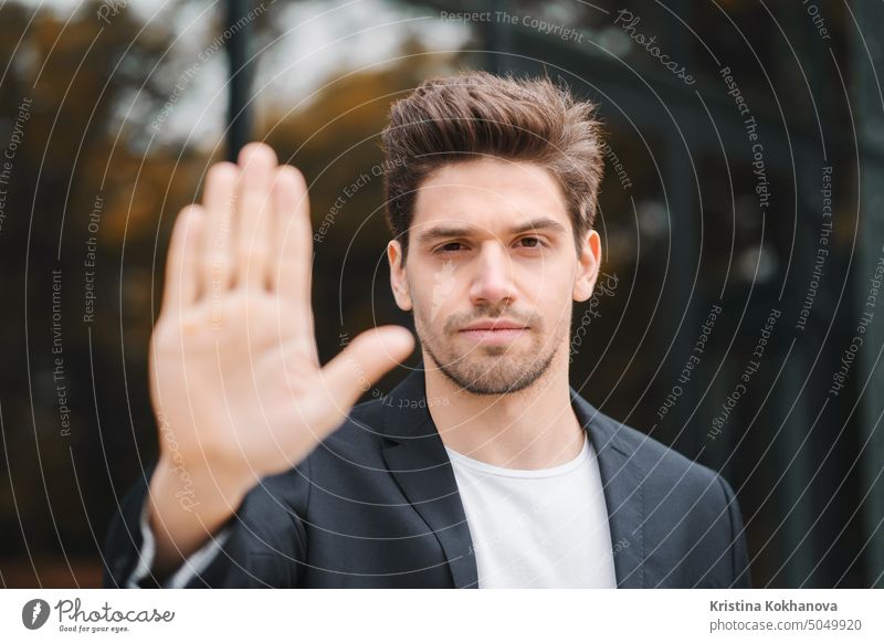 Portrait of young businessman disapproval gesture with hand: denial sign, no sign, negative gesture closes the camera with hand, professional male manager wearing suit jacket.