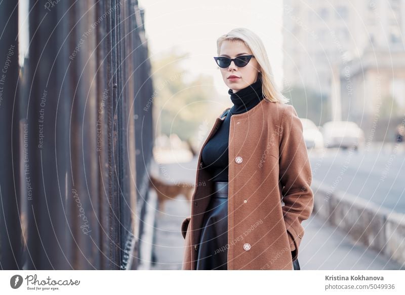 Portrait of young blonde businesswoman in autumn city. Girl have stylish look, sunglasses and nose piercing. Lady walking on the street alone. Fashion concept