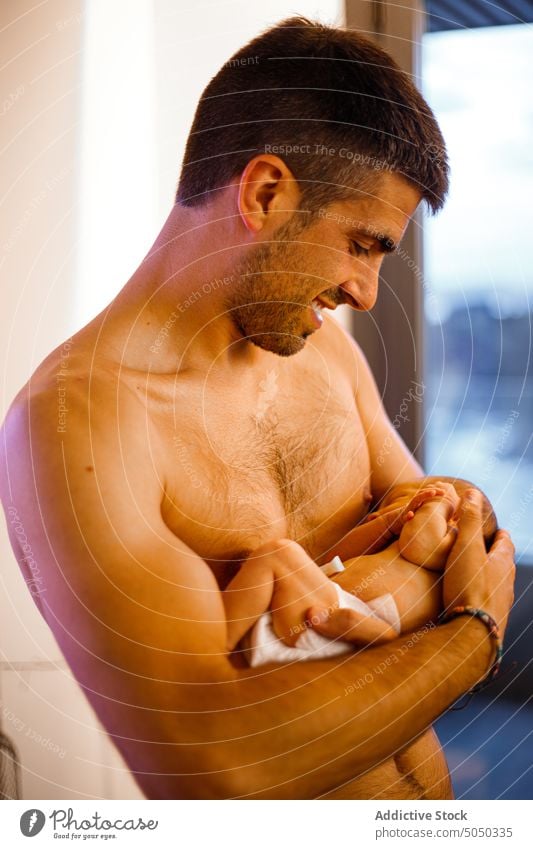 Shirtless man holding newborn baby in arms father infant love care gentle parenthood happy home diaper tender childhood together bonding cute smile adorable