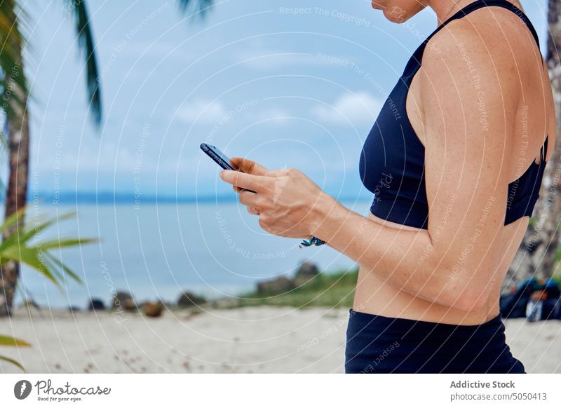 Anonymous woman checking smartphone on tropical beach amazed vacation using summer excited laugh seashore holiday message female gadget ethnic hispanic mobile