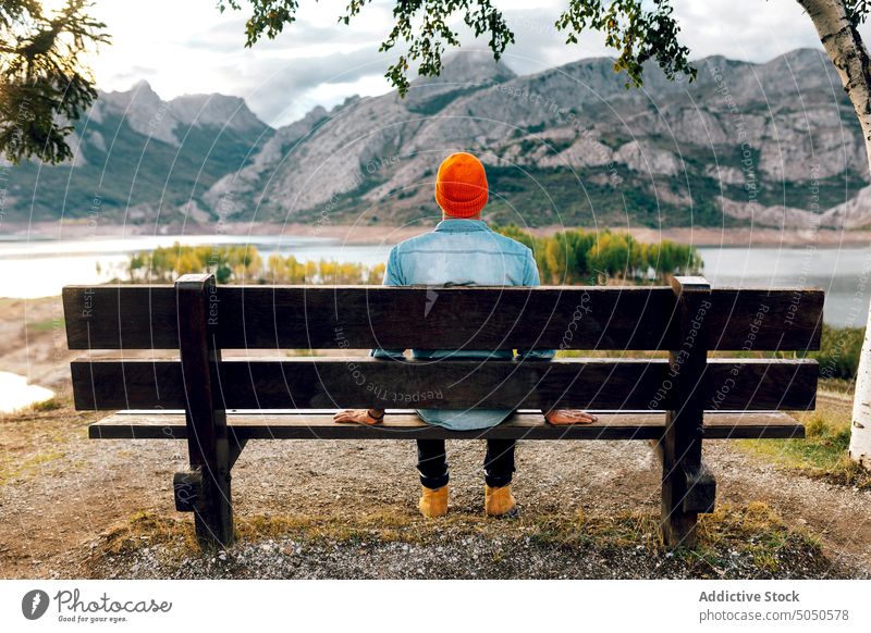Anonymous tourist resting on bench man traveler mountain admire journey observe contemplate trip chill vacation cloudy spectacular lake male tourism picturesque
