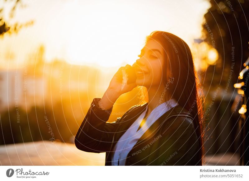 Business woman with smartphone close up in autumn city, sunset light. Girl have conversation with cell phone. Beautiful caucasian young woman talking with mobile device
