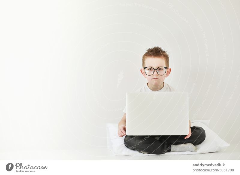 schoolboy in glasses using laptop sitting on bed. Child doing school homework and seriously and tired looking on camera.Online learning, distance lesson, education with online tutor at home isolation