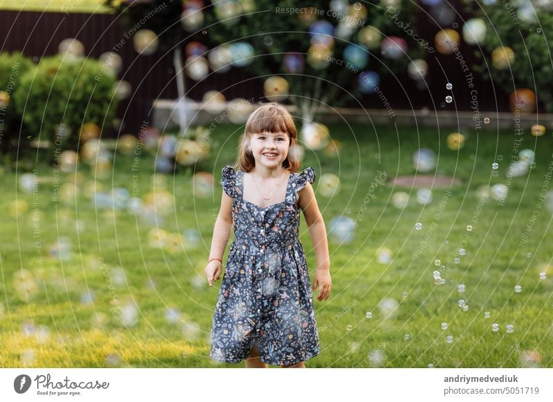 smiling child girl enjoying playing with soap bubbles outdoors on summer day. Cute kid child catches soap bubbles in nature. happy childhood concept fun